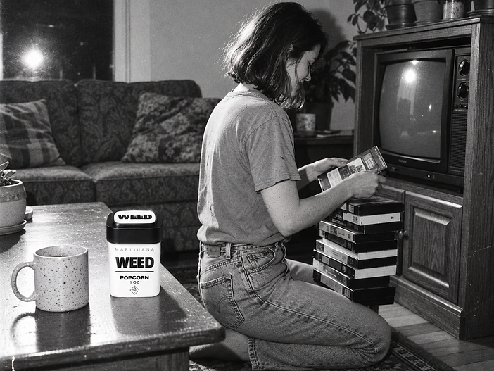 Black-and-white photo of a woman browsing VHS tapes in a living room, with a WEED Popcorn jar on the coffee table