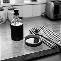 Unlabeled dark glass bottle of infused olive oil beside a small dish and gingham towel