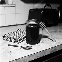 Unlabeled glass jar of homemade honey beside a honey dipper and gingham towel