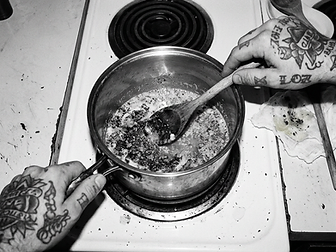 Tattooed hands stirring infused butter in a saucepan on an electric stove