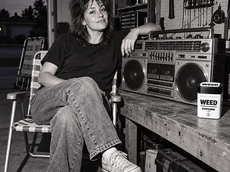 Black-and-white photo of a woman in a garage beside a vintage boombox, with a WEED Popcorn jar on the workbench
