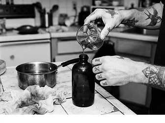 Adult hands pouring homemade infused olive oil into a dark glass bottle in a home kitchen