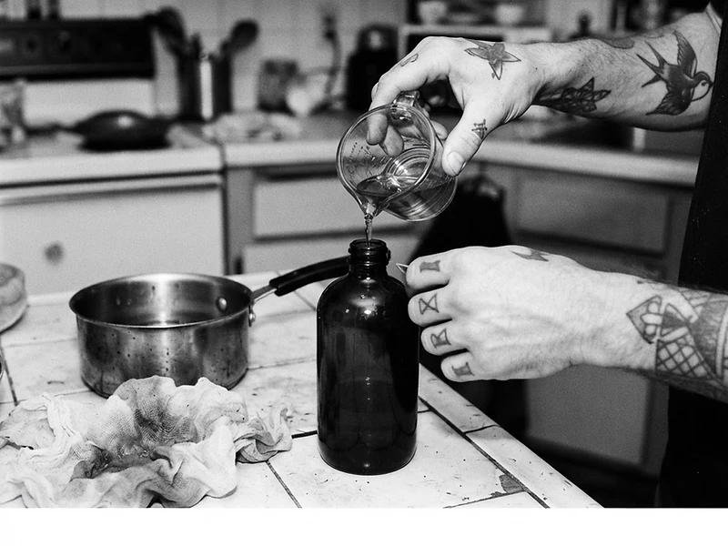 Adult hands pouring homemade infused olive oil into a dark glass bottle in a home kitchen