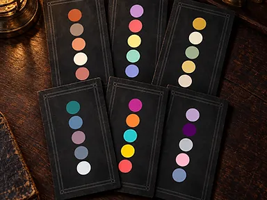 Six black palette cards, each printed with five colour swatches, laid out on a dark wooden desk beside a brass lantern.