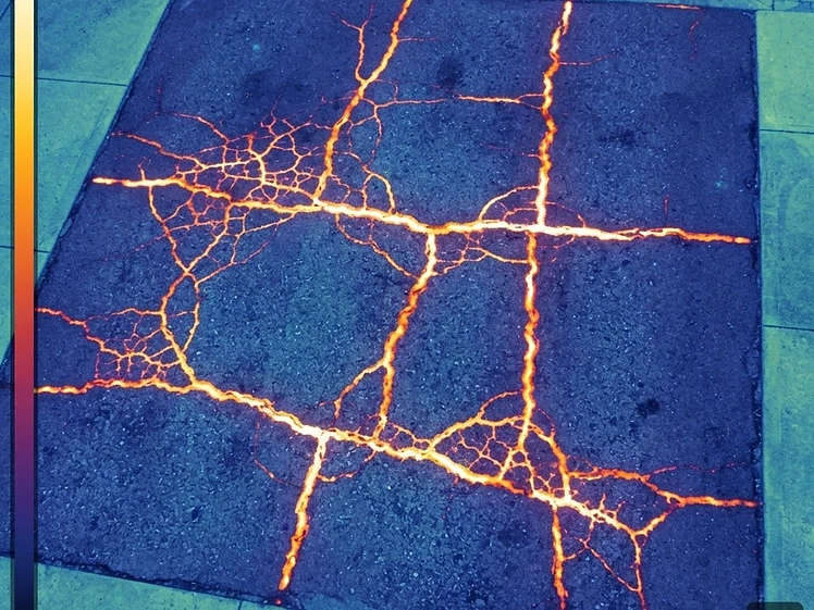 Thermal infrared view of freshly sealed driveway cracks glowing warm against cold pavement