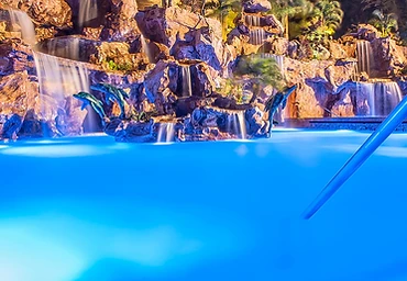 Resort pool with illuminated waterfalls at night