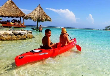 Two guests paddling a red kayak in the clear shallows
