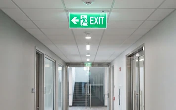 Illuminated green emergency exit sign on a commercial building ceiling