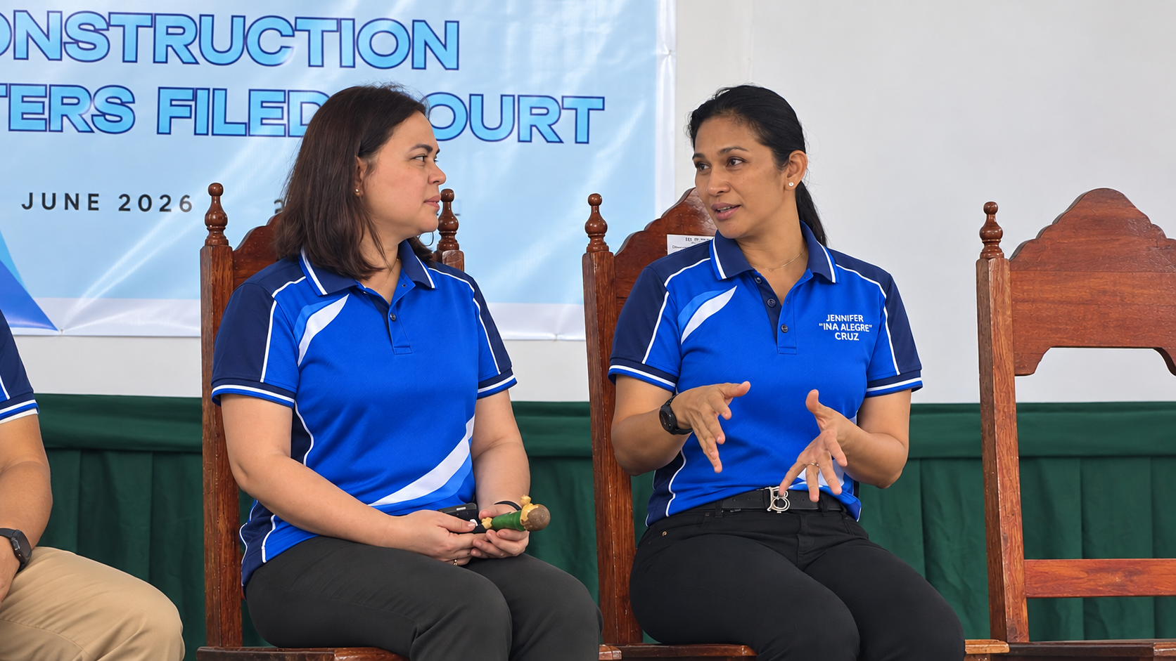 Mayor Jennifer Mindanao-Cruz speaking while seated beside another guest at a program with a printed backdrop.