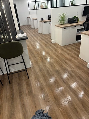 Plancher en cours de nettoyage près de postes de travail et d’une cuisinette.