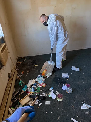 Personne en combinaison de protection ramassant les déchets au sol dans un logement.
