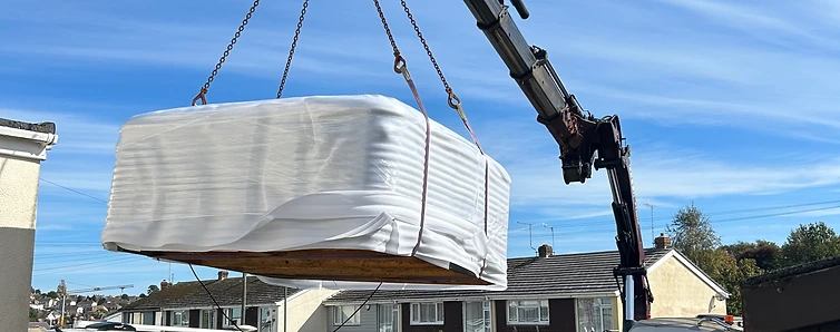 Hot tub lifted by a crane over a garden fence