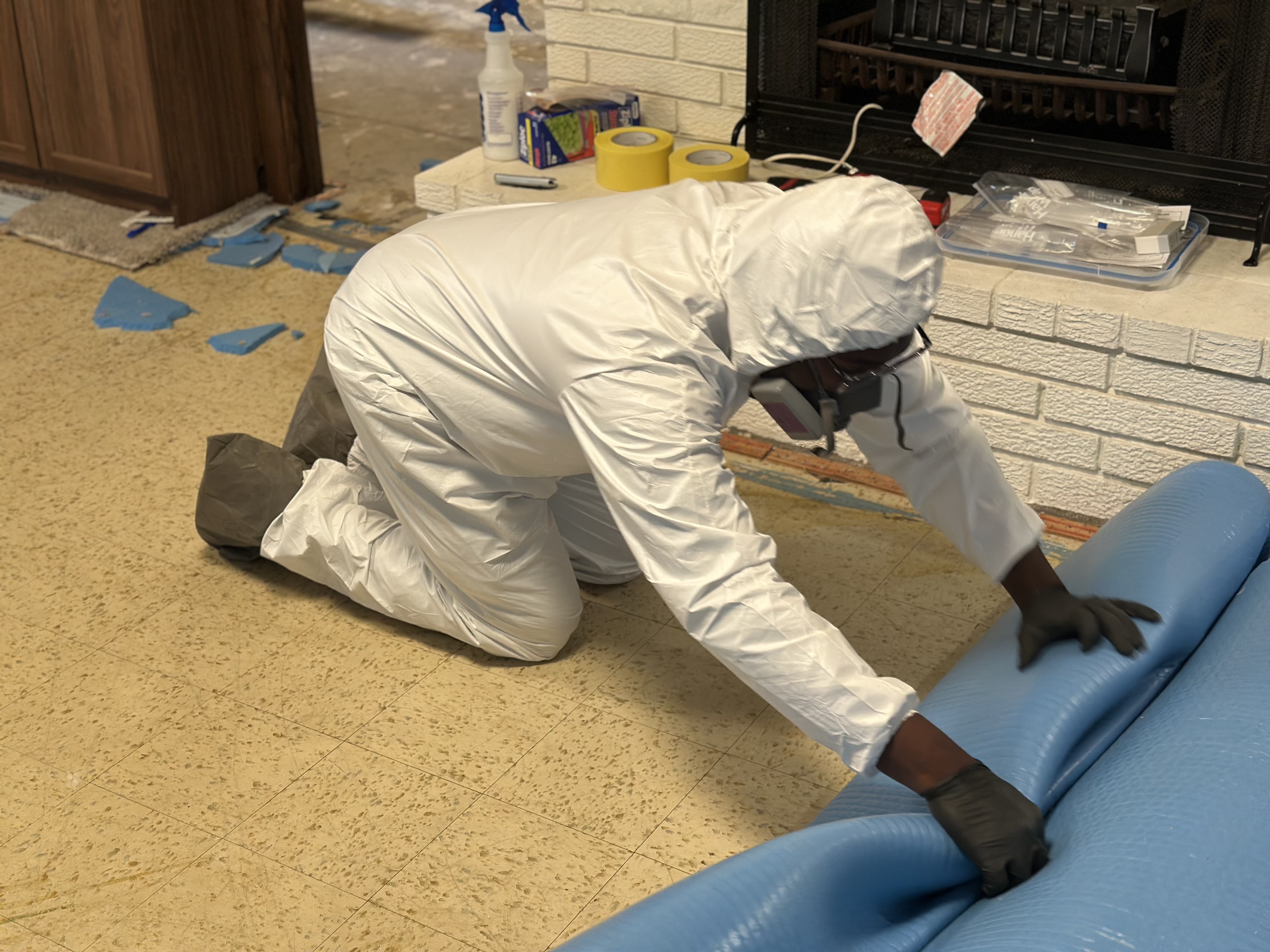 Technician kneeling to roll up blue plastic sheeting near a fireplace