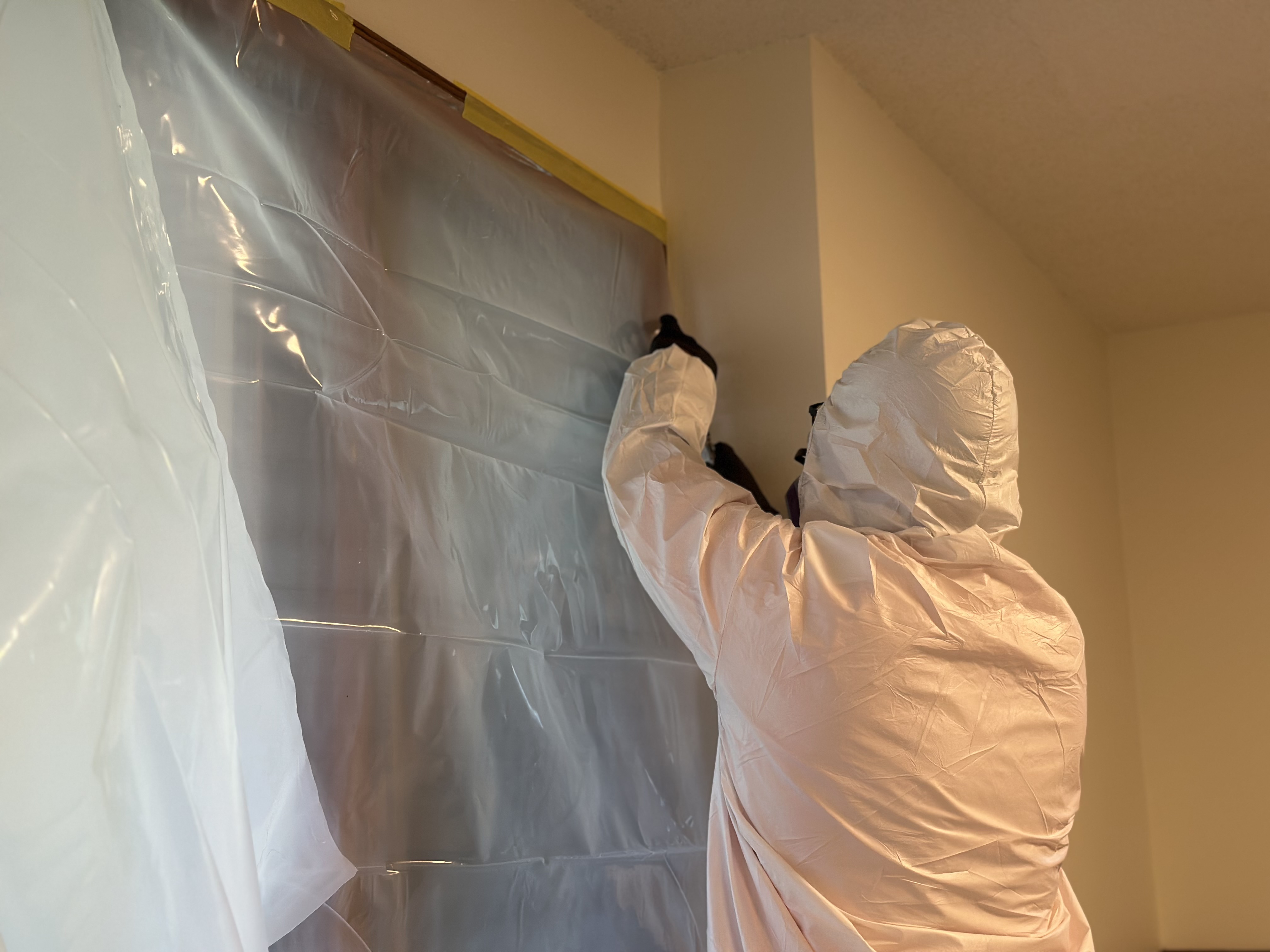 Technician securing clear plastic containment sheeting to a wall