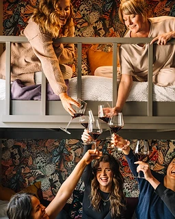 Five women toasting glasses of red wine together in a bunk bed