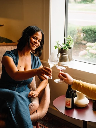 Michele smiling and raising a glass of wine by the window
