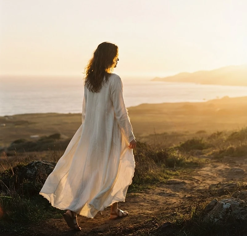 A woman in flowing ivory fabric stepping into golden morning light