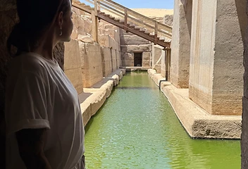 A figure standing at the end of a green pool within the ruins