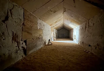 A figure in white seated in a dim ancient corridor