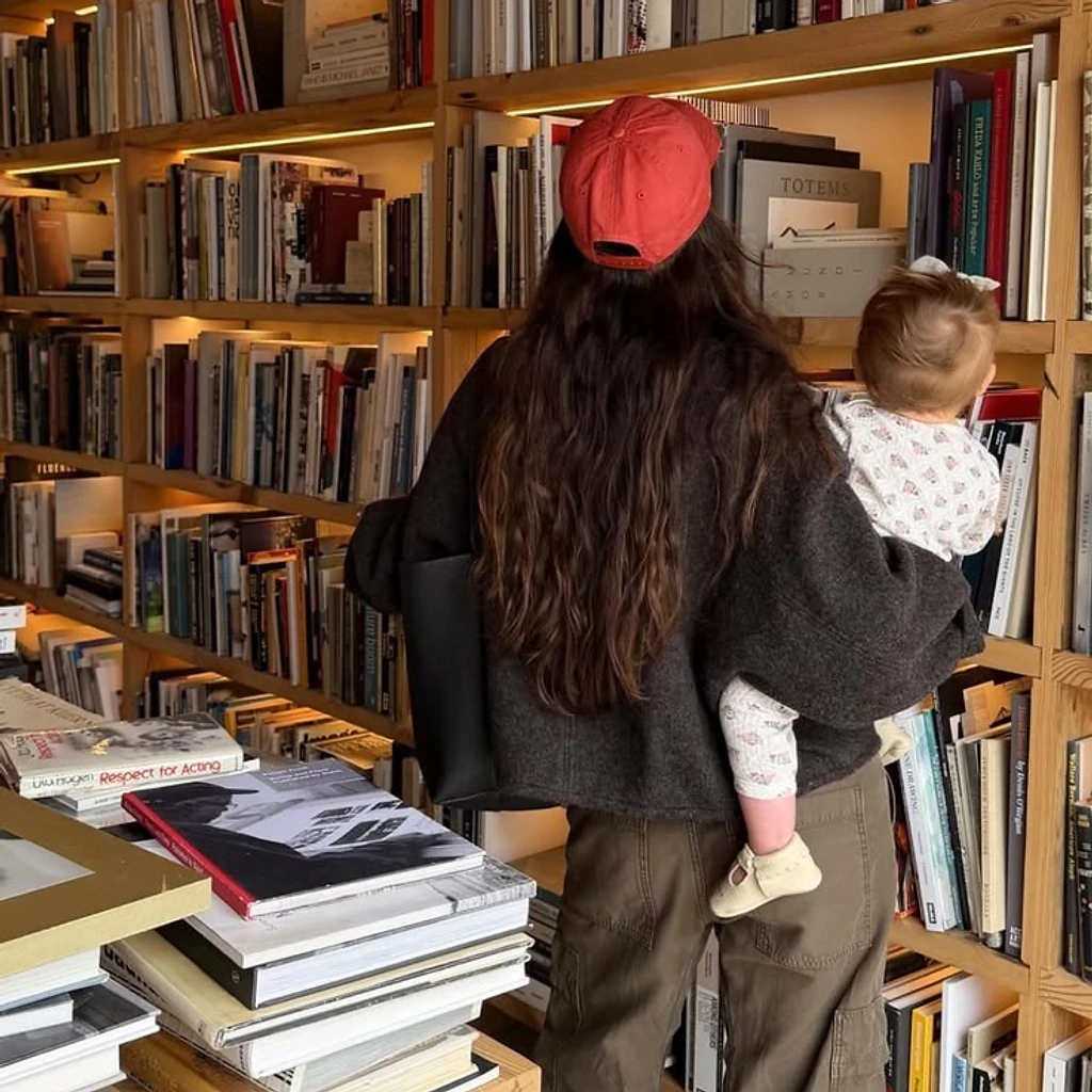 A mother carrying her child through a warm, wood-shelved bookshop