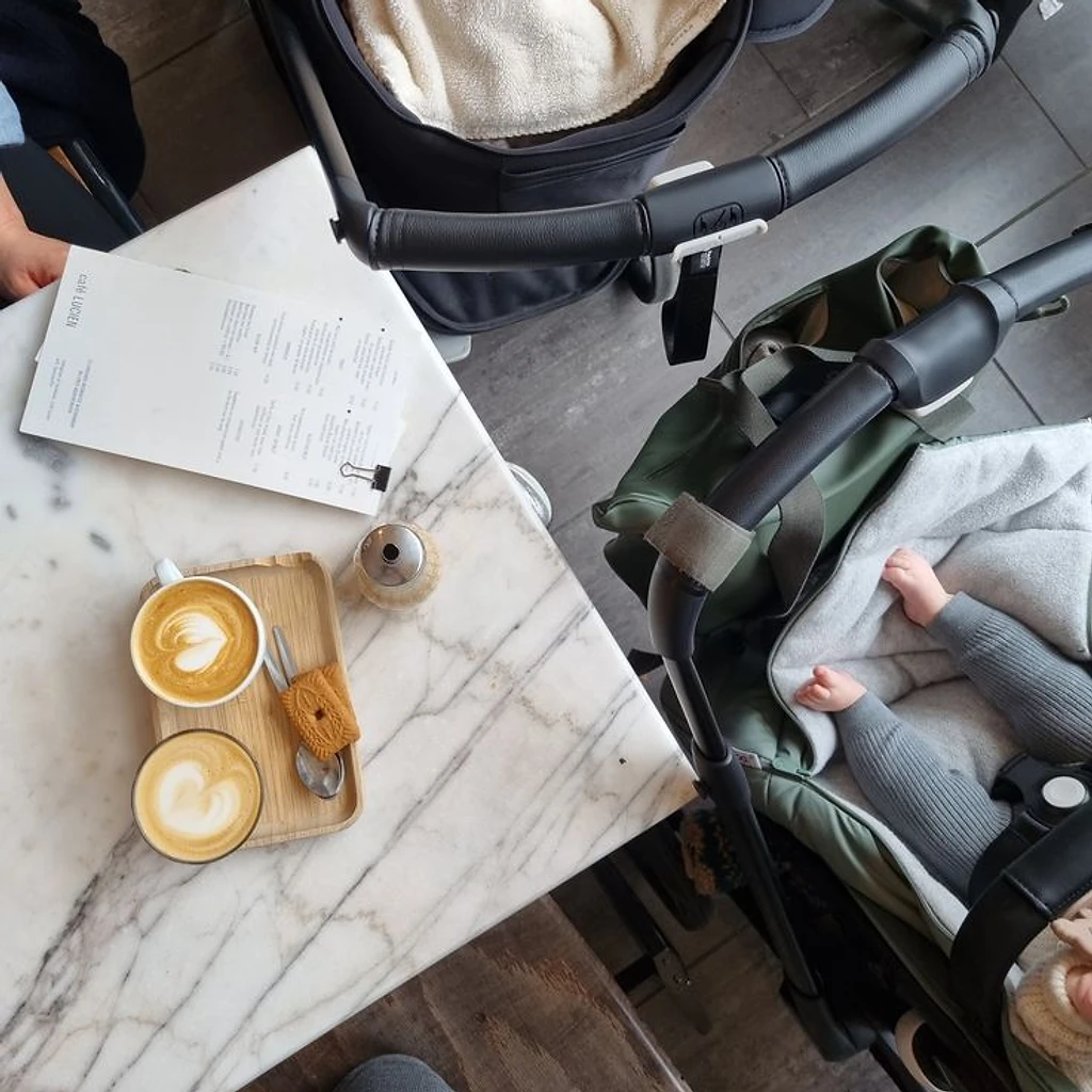 Two lattes on a marble café table beside a stroller
