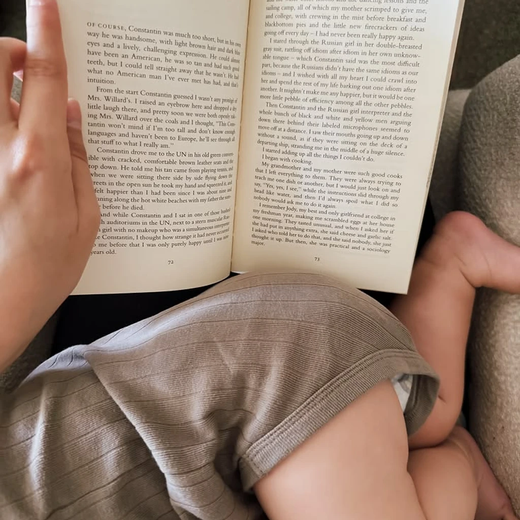 An open book held in one hand with a baby resting on the reader's lap