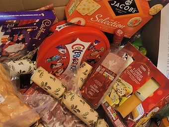 An open hamper box filled with fresh food, cheese, crackers, chocolates and a letter from the charity