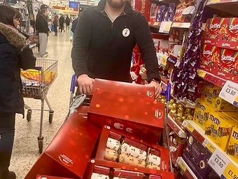 A volunteer with a trolley full of Christmas crackers and treats in a supermarket