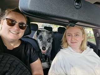Two friends and a blue heeler pup grinning from the back seat on a group outing