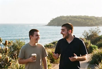 Django, a support worker, laughing with a participant as they walk a sunny coastal path