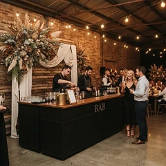 Matte black bar at a warehouse dinner party with draped cream linen, dried flowers and wood slatting