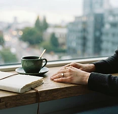 Hands beside a quiet journal and cup at a window suggest a mindful decision-making moment