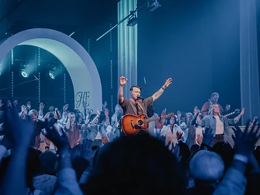 Worship leader playing guitar with the crowd raised in worship