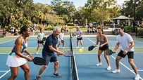 Grupo de personas sonriendo mientras juegan a pickleball en una pista al aire libre