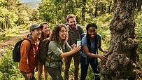 Grupo de amigos sonriendo mientras buscan un geocache en un bosque soleado.