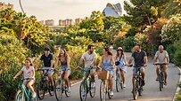 Grupo de amigos montando en bicicleta por el Jardín del Turia en Valencia con luz de atardecer.