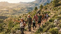 Grupo de personas diversas caminando por una ruta de montaña en España con mochilas y ropa técnica de senderismo.