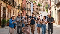 Grupo de personas con cámaras fotográficas caminando y charlando por una calle histórica soleada