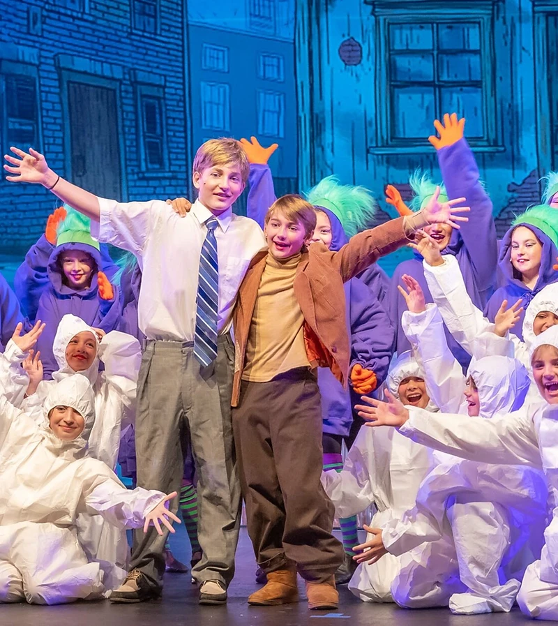 Wonka cast members reaching outward under blue stage light