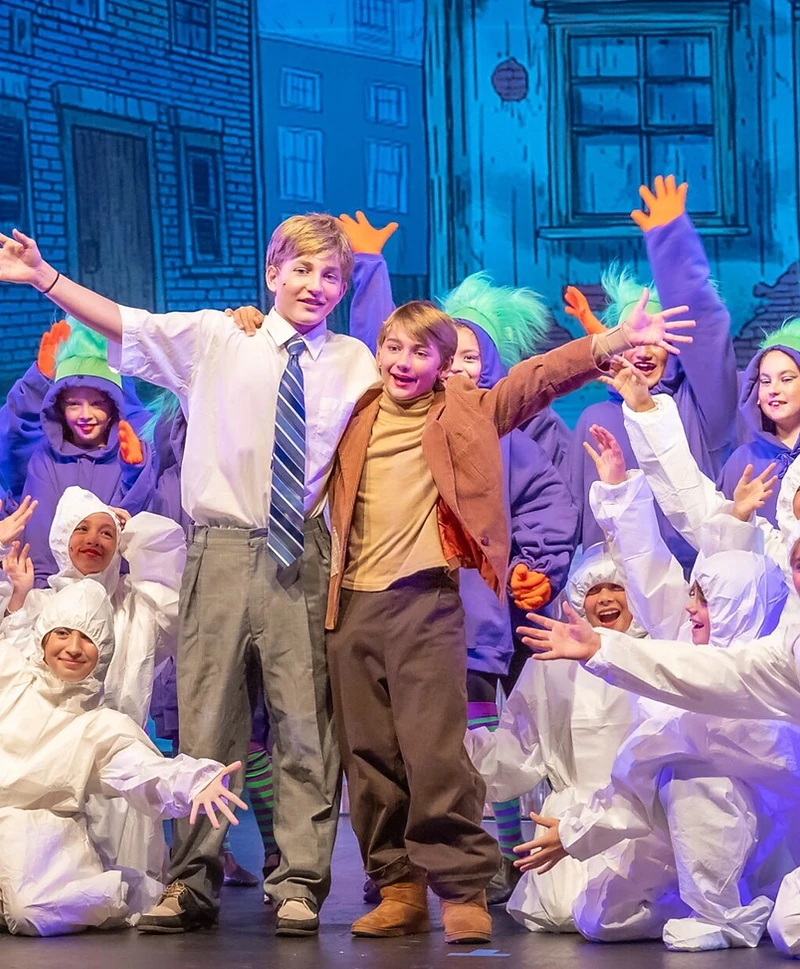Wonka cast members reaching outward under blue stage light