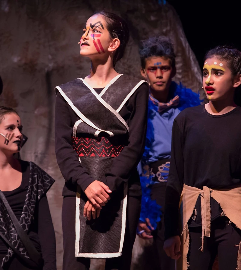 A Lion King ensemble in costume on a darkened stage