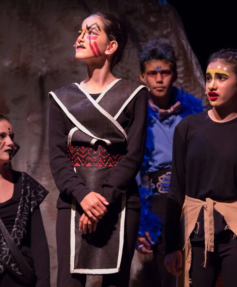 A Lion King ensemble in costume on a darkened stage