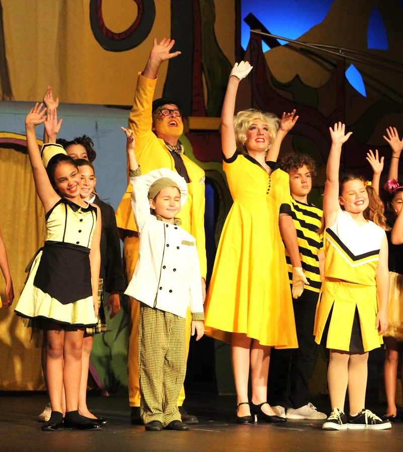 Seussical cast in bright yellow costumes waving on stage