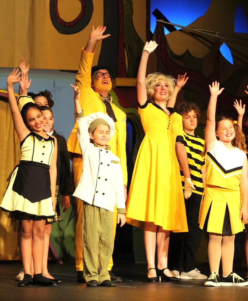 Seussical cast in bright yellow costumes waving on stage
