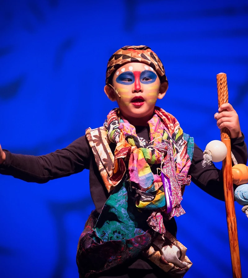 A young Lion King performer holding a staff under blue light