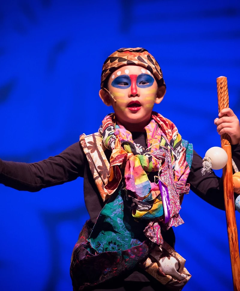 A young Lion King performer holding a staff under blue light
