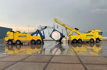 Twee kranen van Betten Sneek tillen samen een containerdrager met ketel op een nat industrie terrein