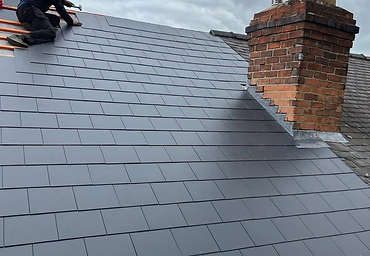 Roofer finishing a new grey slate roof beside a chimney