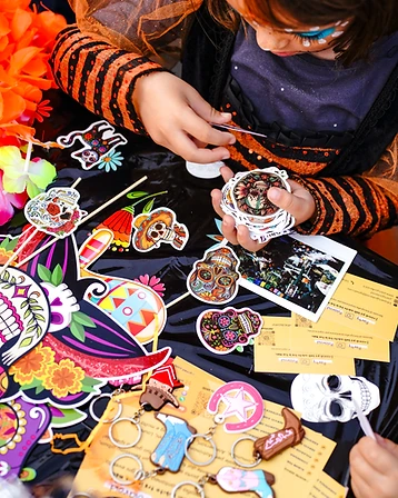 Bambini con trucco dipinto che scelgono calaveras e decorazioni colorate su un tavolo della festa.
