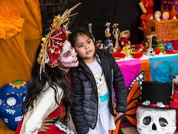 Un partecipante con trucco da Catrina e un bambino davanti all'ofrenda, durante il Día de los Muertos Roma 2025.